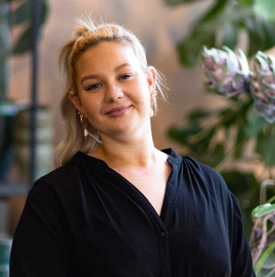 Eine Frau in einem schwarzen Hemd steht vor Pflanzen. {{brizy_dc_image_alt imageSrc=