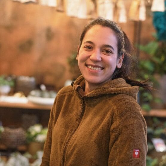 Eine Frau in einer braunen Jacke steht vor einem Blumenladen.