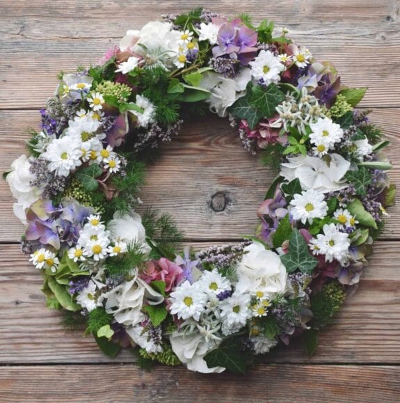 Ein Kranz aus Blumen auf einem Holztisch. {{brizy_dc_image_alt imageSrc=